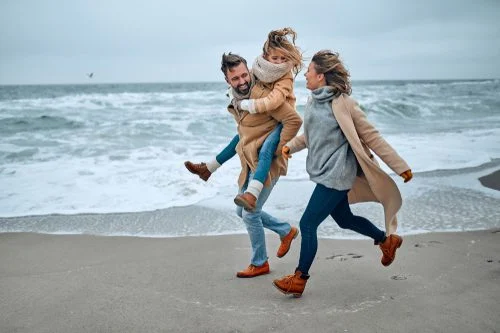 A mom, dad, and daughter run on the beach during the winter in Old Saybrook, CT.