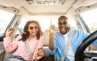 A couple smiles in their vehicle, seatbelts buckled, during a New England road trip to Old Saybrook, CT.