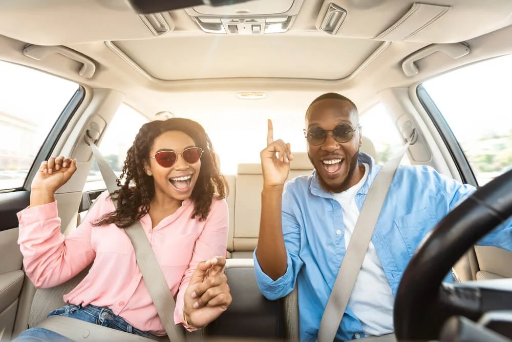 A couple smiles in their vehicle, seatbelts buckled, during a New England road trip to Old Saybrook, CT.